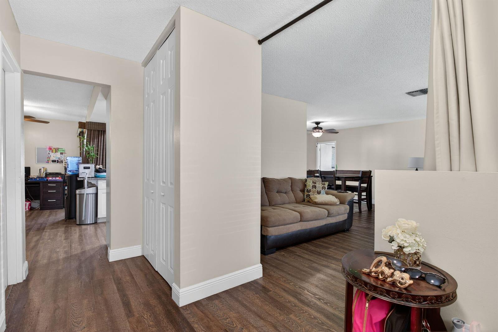 A living room with wood-look flooring, a brown sofa, and a white bi-fold closet door — 6701 NW 20th Street, Margate FL 33063, MARGATE, FL