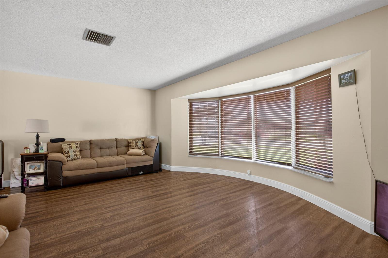 A living room features wood-look flooring, a brown sofa, and a large bay window — 6701 NW 20th Street, Margate FL 33063, MARGATE, FL