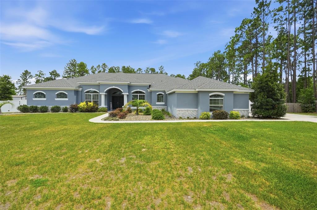 A single-story gray house with a stone-accented facade sits on a large grassy lot — 4743 JUMPER LOOP, SPRING HILL, FL