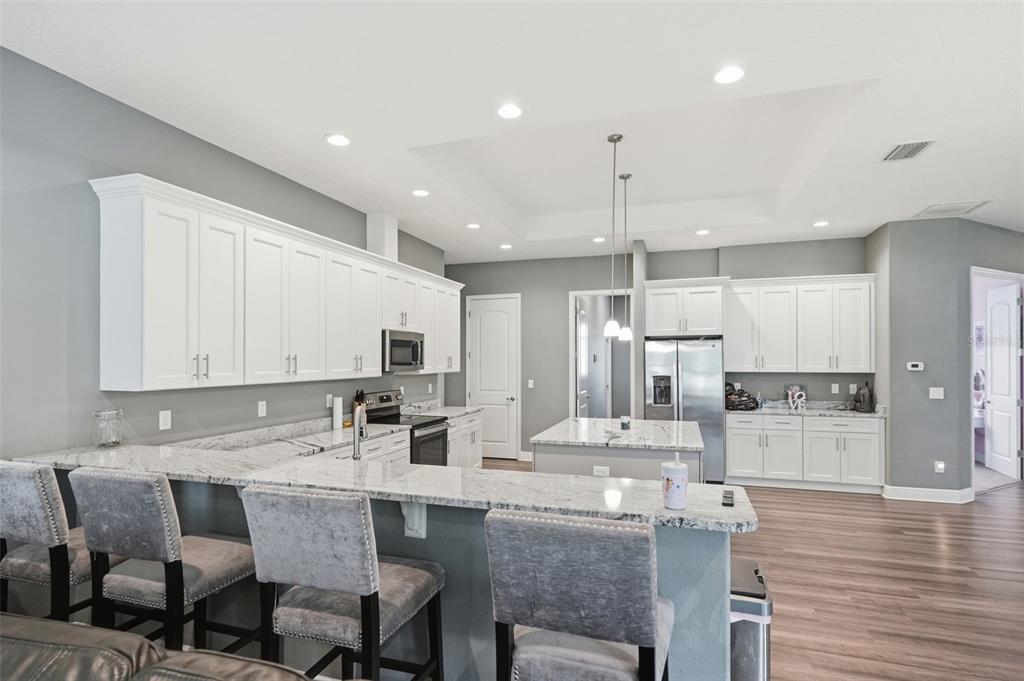 A modern kitchen features white cabinets, granite countertops, a center island, and gray bar stools — 4743 JUMPER LOOP, SPRING HILL, FL