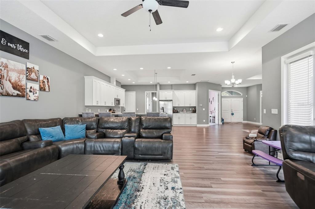 A spacious open-concept living room features a dark leather sectional, white kitchen cabinetry, and wood-look flooring — 4743 JUMPER LOOP, SPRING HILL, FL