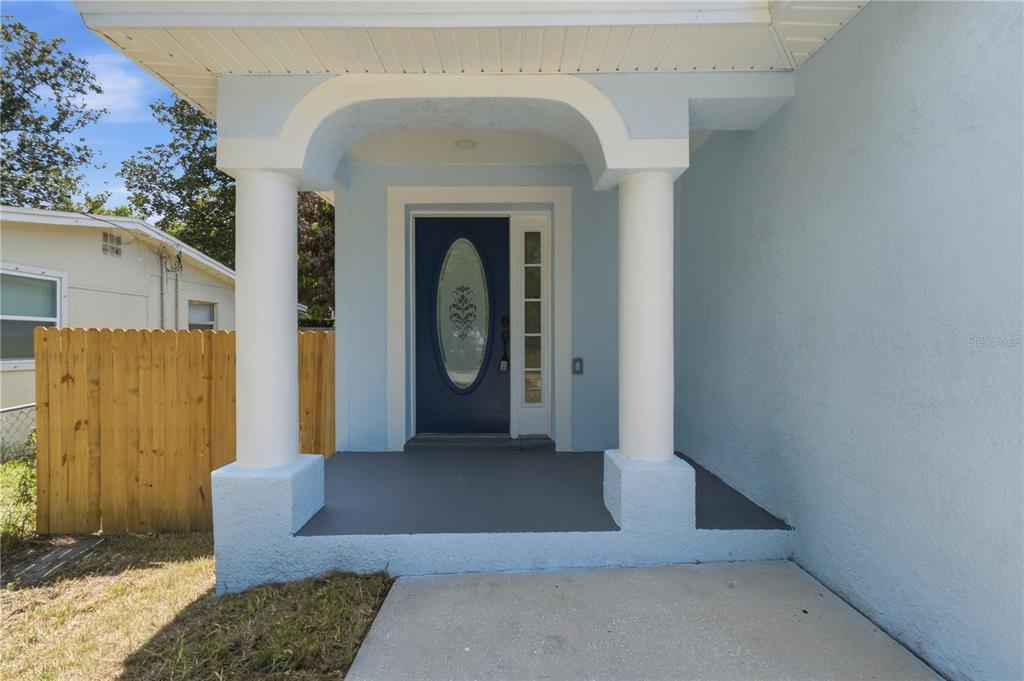 A covered front porch features two white columns, a blue door, and a concrete floor — 6812 LYMAN AVENUE, TAMPA, FL