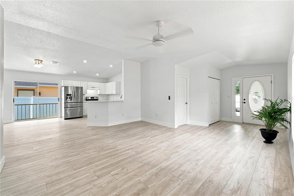 A bright, open-concept living area features light wood-look flooring, a kitchen, and a front door — 6812 LYMAN AVENUE, TAMPA, FL