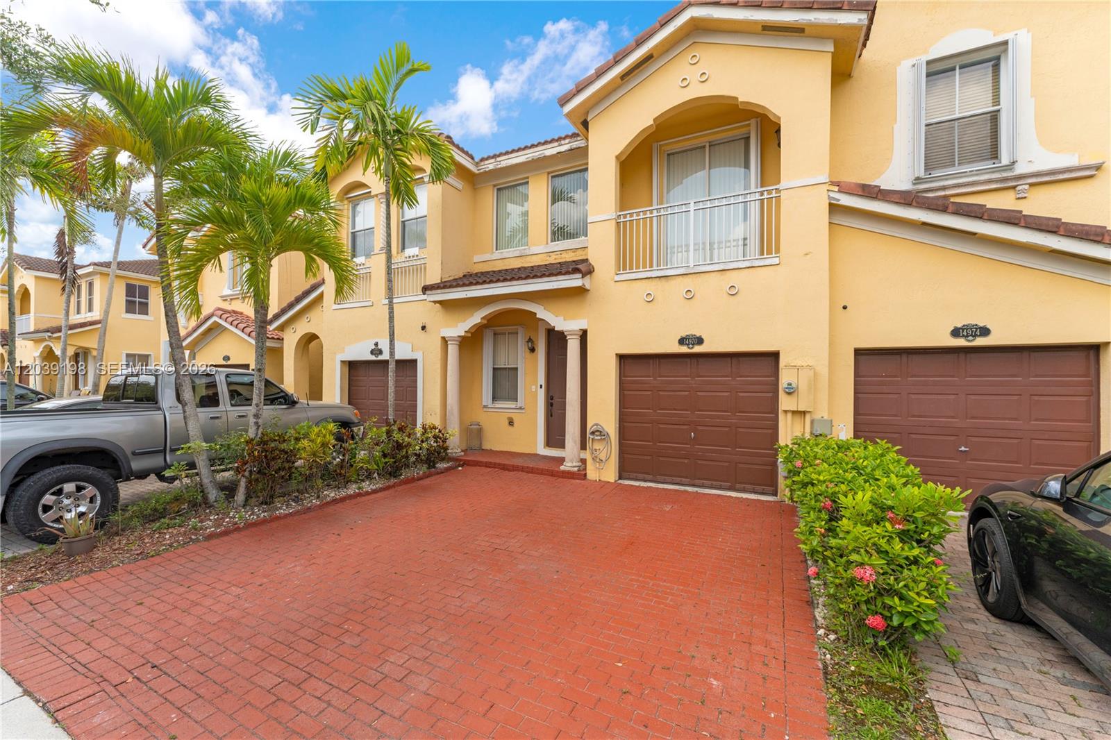A yellow two-story townhouse features a red brick driveway, a garage, and palm trees — 14970 SW 9th Ter, Miami FL 33194, MIAMI, FL