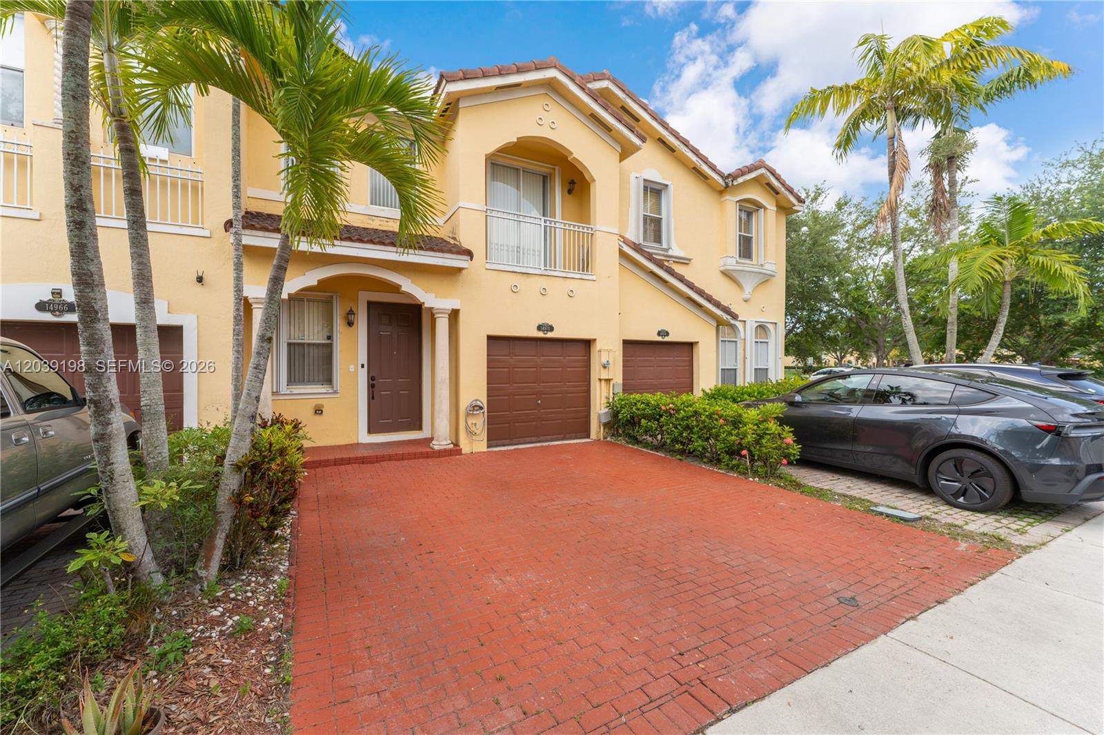 A two-story yellow stucco townhouse features a brick driveway, brown garage doors, and palm trees — 14970 SW 9th Ter, Miami FL 33194, MIAMI, FL