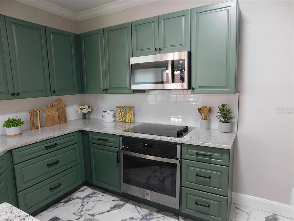 A kitchen features sage green cabinets, white subway tile backsplash, and speckled granite countertops — 2725 VIA CIPRIANI UNIT 735B, CLEARWATER, FL