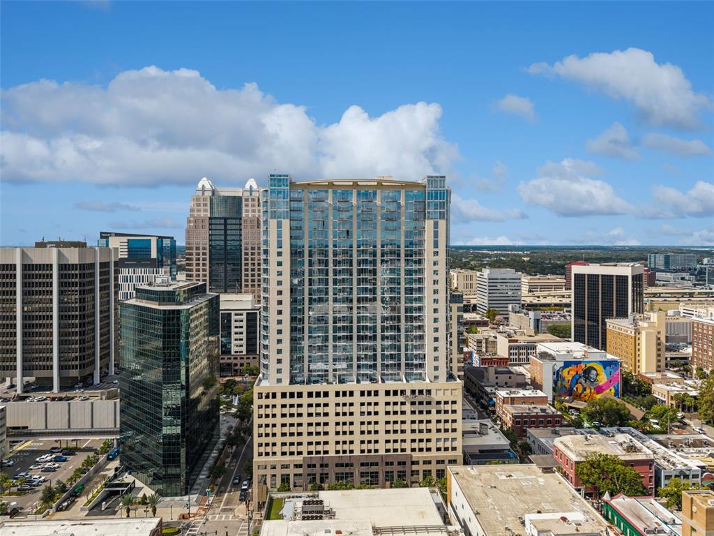 An aerial view of a tall glass residential tower surrounded by other urban office buildings — 155 S COURT AVENUE UNIT P-2901, ORLANDO, FL