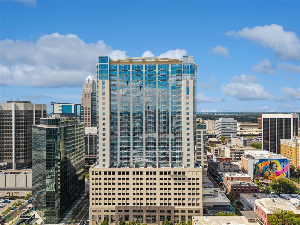 An aerial view of a tall glass-faced residential tower surrounded by other city buildings — 155 S COURT AVENUE UNIT P-2901, ORLANDO, FL