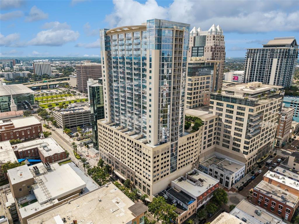 An aerial view of a tall glass residential skyscraper surrounded by urban buildings and streets — 155 S COURT AVENUE UNIT P-2901, ORLANDO, FL