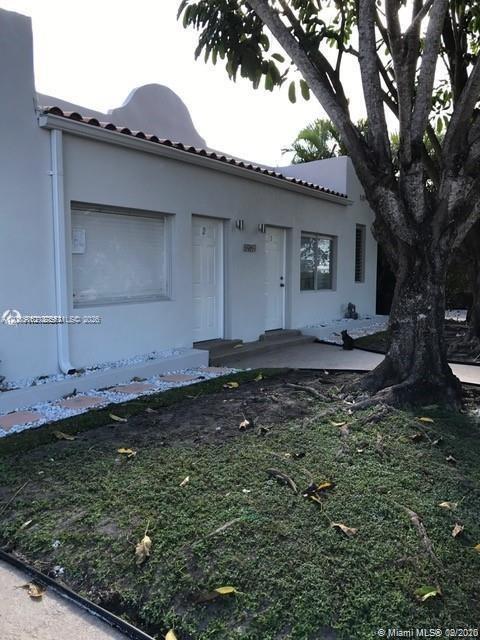 A low-rise building with two white doors and a large tree in the front yard — SURFSIDE, FL