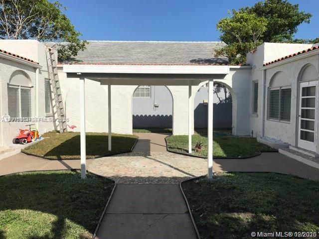 A white house features a covered patio area between two wings with a paved walkway — SURFSIDE, FL