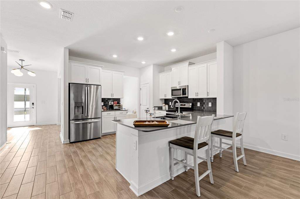 A modern kitchen features white cabinets, stainless steel appliances, a dark island, and wood-look flooring — 11442 LISTENING DRIVE, ORLANDO, FL