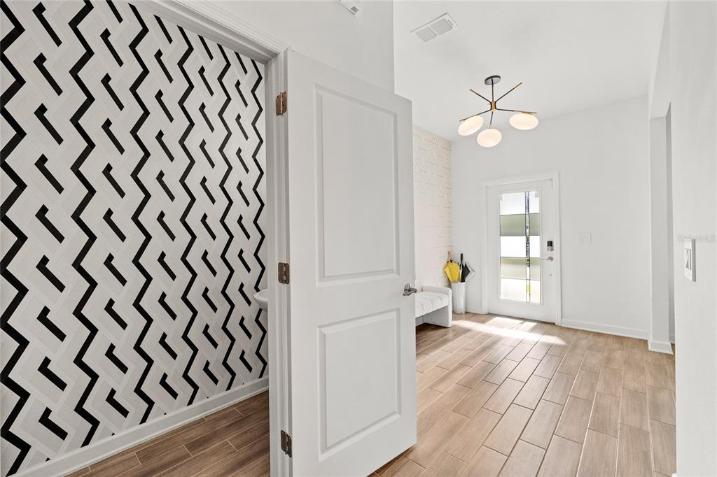 An entryway features light wood-look tile flooring, a modern chandelier, and a geometric-patterned accent wall — 11442 LISTENING DRIVE, ORLANDO, FL