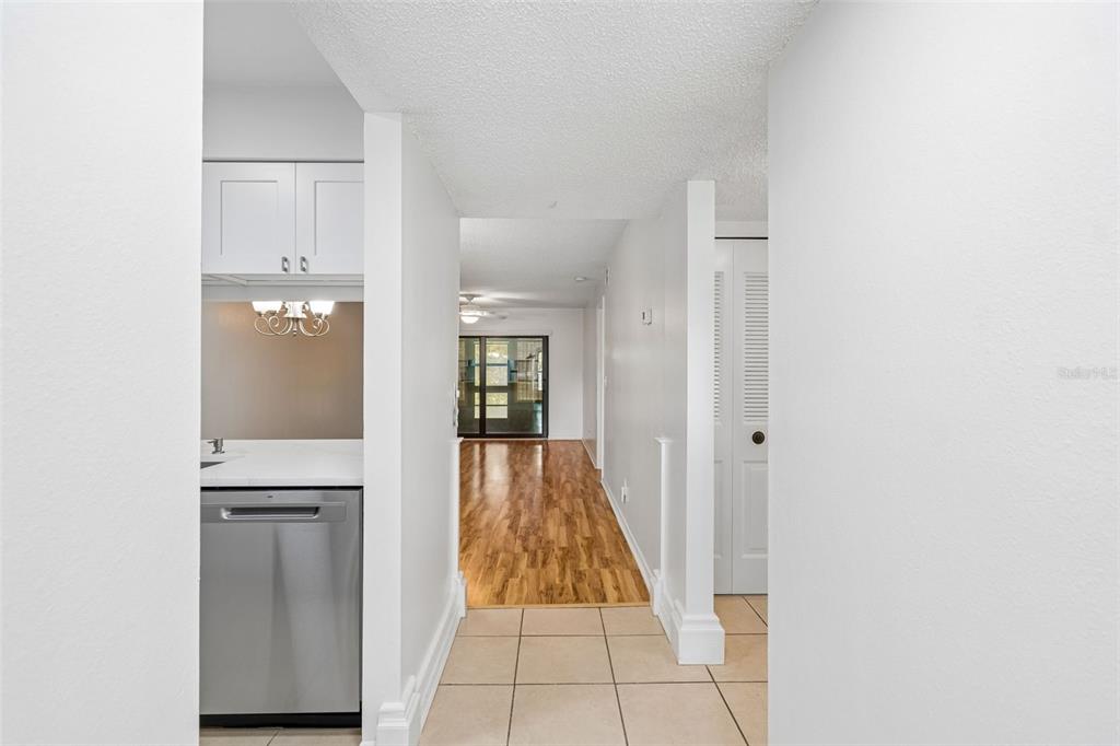 A hallway with tile flooring leads to a living area with wood floors and sliding doors — 723 83RD AVENUE N UNIT 104, ST PETERSBURG, FL
