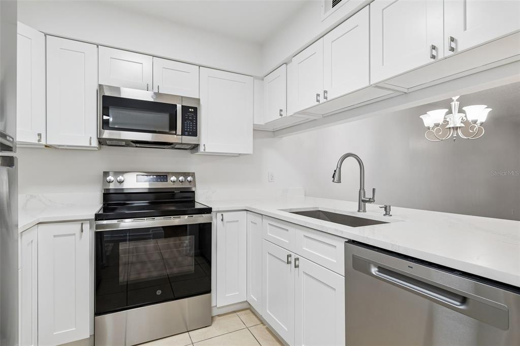 A kitchen features white cabinets, stainless steel appliances, a white countertop, and a double-basin sink — 723 83RD AVENUE N UNIT 104, ST PETERSBURG, FL