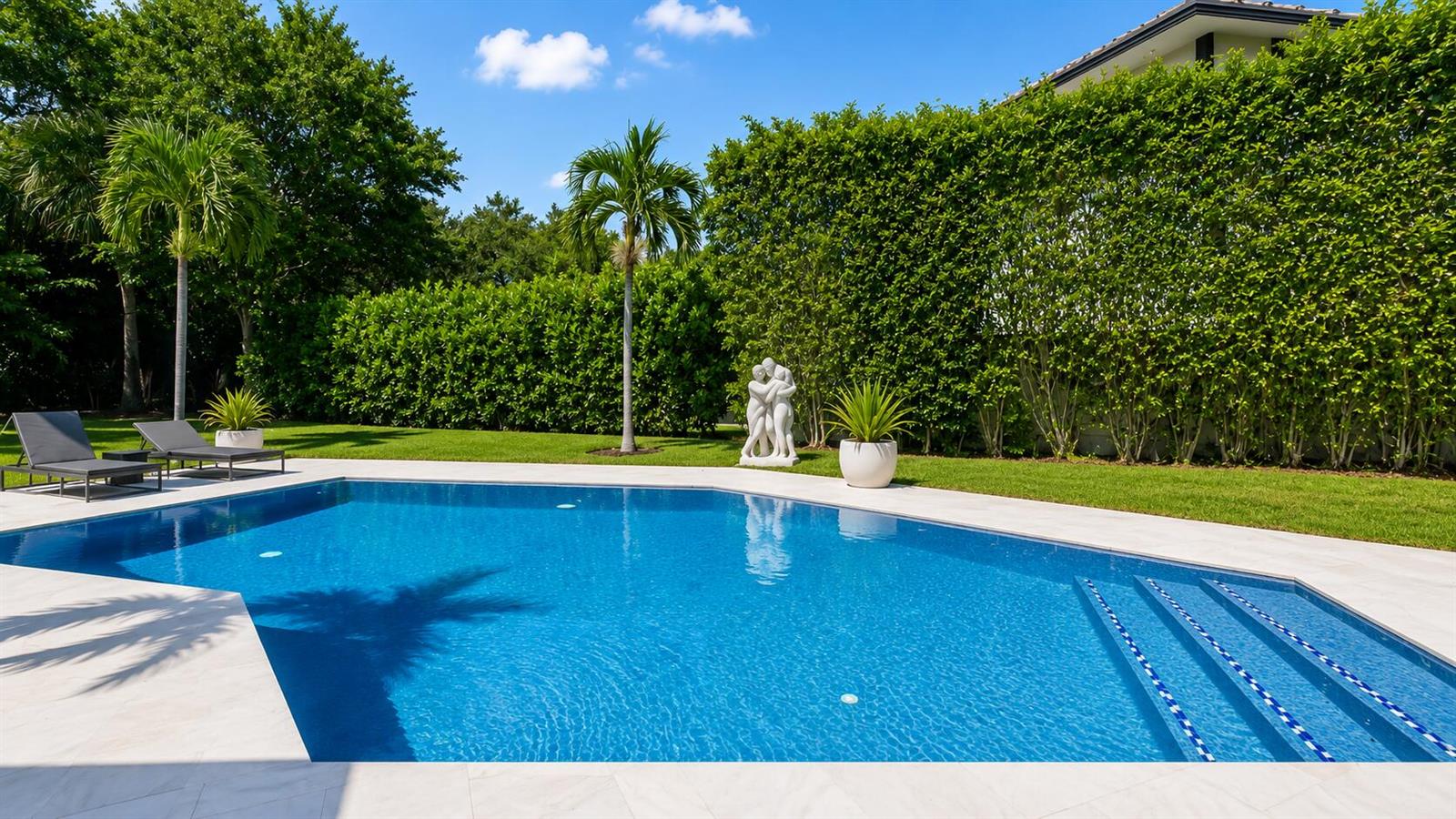 A swimming pool with lounge chairs sits in a backyard bordered by tall green hedges — 501 Sandpiper Way, Boca Raton FL 33431, BOCA RATON, FL