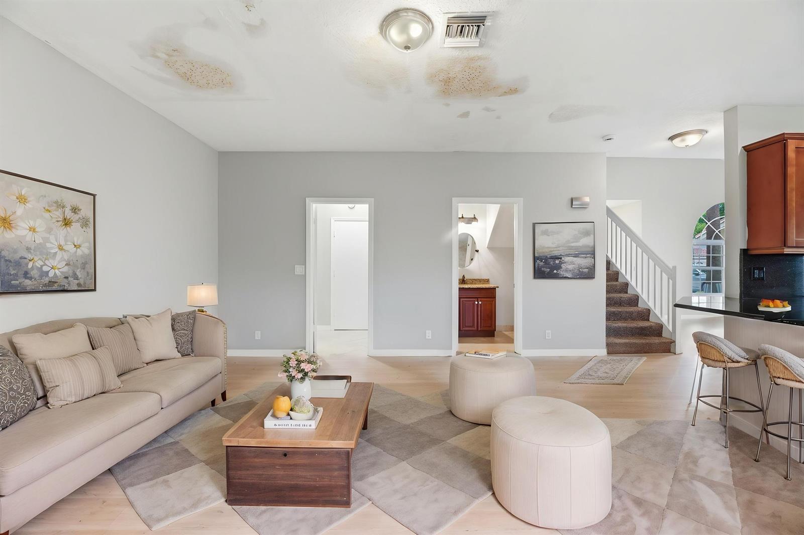 A living room with a beige sofa, coffee table, two ottomans, and water-damaged ceiling stains — 7634 Trenton Drive, Lake Worth FL 33467, LAKE WORTH, FL
