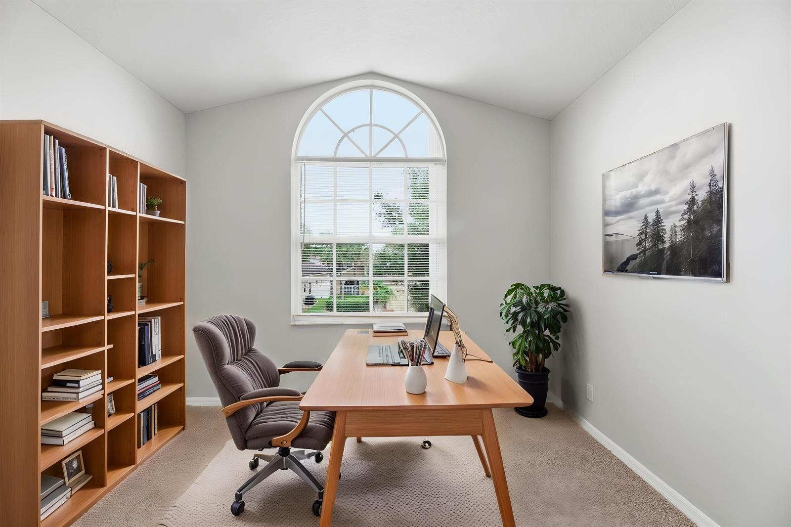 A home office features a wooden desk, a gray chair, a bookshelf, and an arched window — 7634 Trenton Drive, Lake Worth FL 33467, LAKE WORTH, FL
