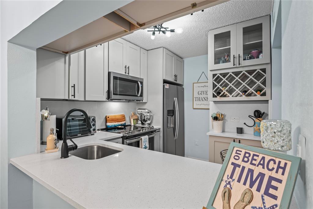 A kitchen features white cabinets, stainless steel appliances, a wine rack, and a breakfast bar — 3232 LAKE PINE WAY UNIT H2, TARPON SPRINGS, FL