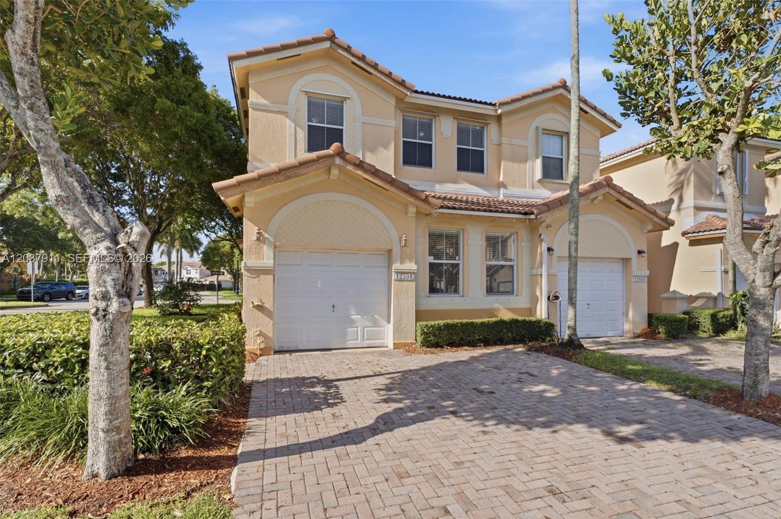 A two-story, beige stucco townhouse with two garage doors and a brick paver driveway — 12594 SW 122nd St, Miami FL 33186, MIAMI, FL