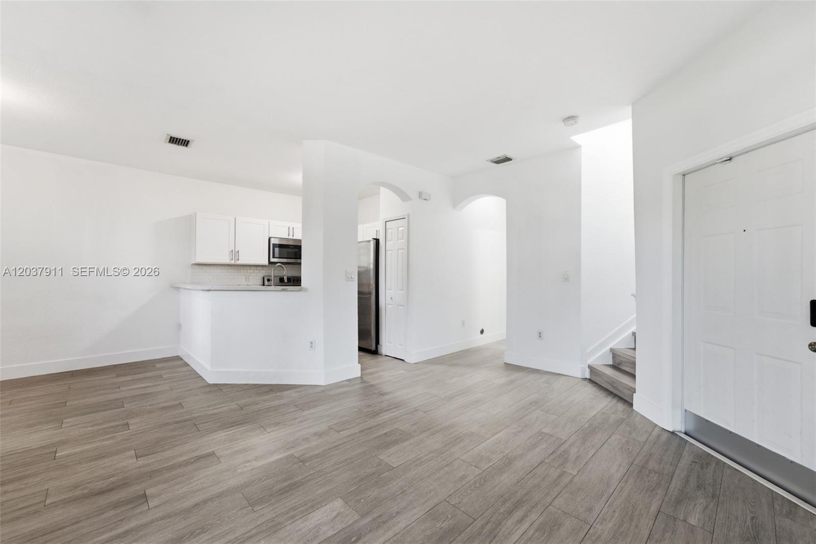 An open-concept living area features light wood-look flooring, white walls, and an adjacent kitchen — 12594 SW 122nd St, Miami FL 33186, MIAMI, FL