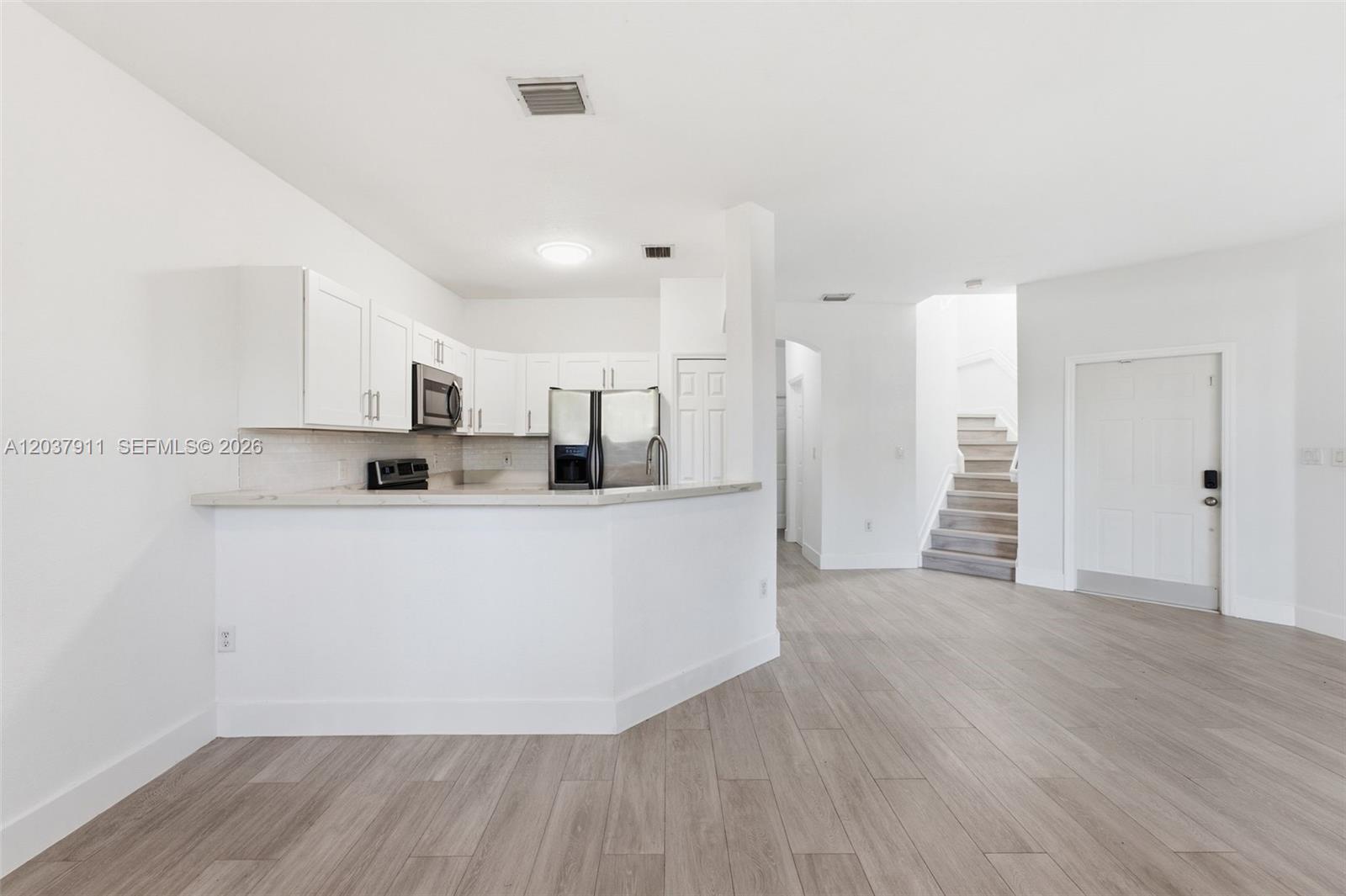 A kitchen with white cabinets and stainless steel appliances overlooks a living area with stairs — 12594 SW 122nd St, Miami FL 33186, MIAMI, FL