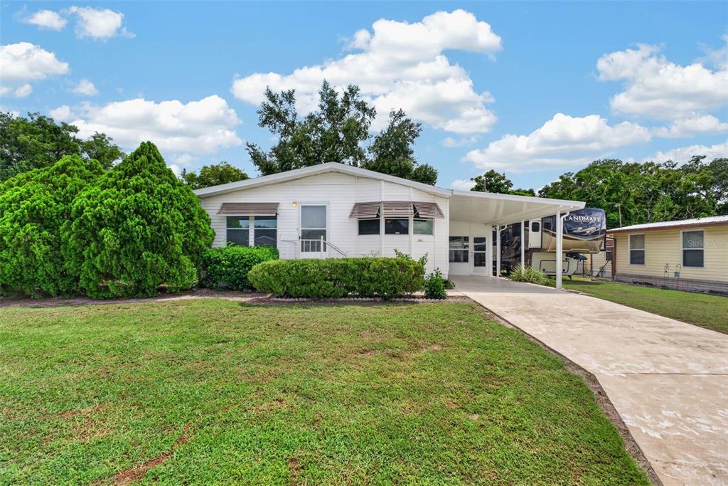 A white single-story house with a carport and a large front lawn — 39200 OLA AVENUE, ZEPHYRHILLS, FL