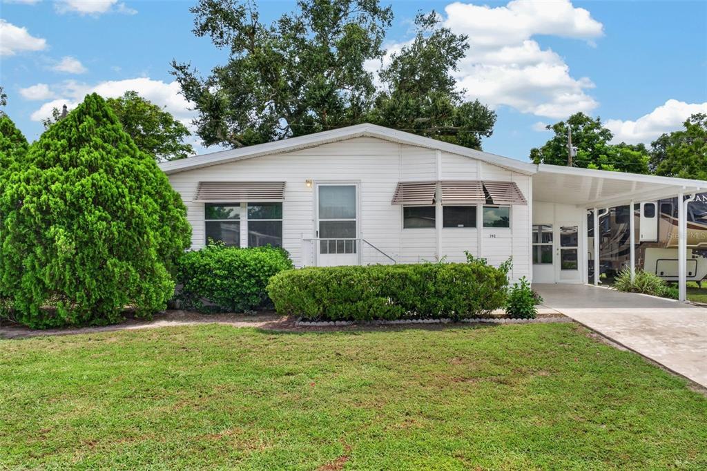 A white single-story manufactured home with a front lawn, hedges, and a covered carport — 39200 OLA AVENUE, ZEPHYRHILLS, FL