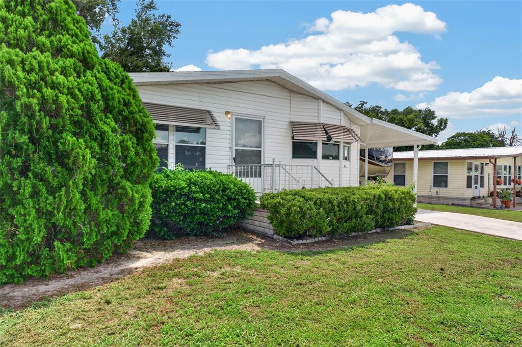 A white mobile home with a metal awning and landscaping sits on a grassy lot — 39200 OLA AVENUE, ZEPHYRHILLS, FL