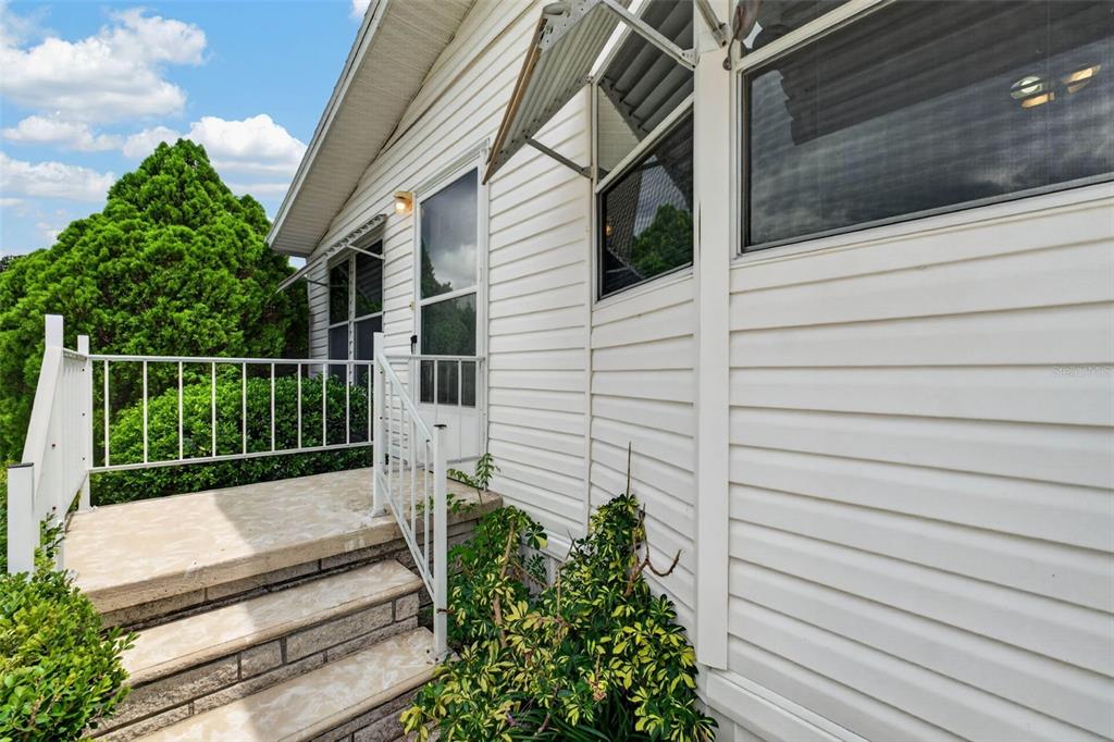 Exterior view of a white-sided home with a concrete porch, metal railings, and stairs — 39200 OLA AVENUE, ZEPHYRHILLS, FL
