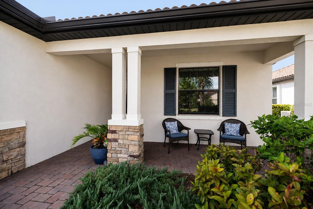 A covered front porch features stone-based columns, brick pavers, two chairs, and a small table — 19393 CRUISE DRIVE, VENICE, FL
