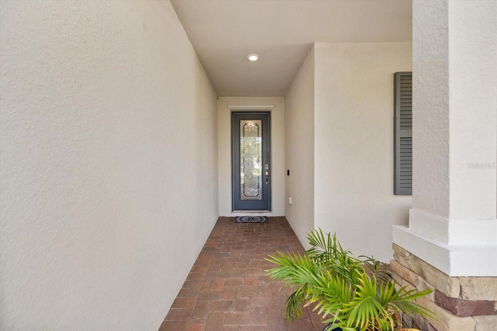 A covered entryway features a brick-paved floor, a gray front door, and a potted plant — 19393 CRUISE DRIVE, VENICE, FL