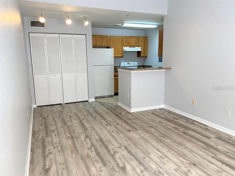 A kitchen with wood cabinets and white appliances opens to a room with wood flooring — 9045 LEE VISTA BOULEVARD UNIT 1502, ORLANDO, FL