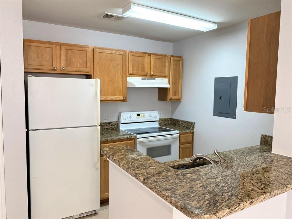 A kitchen features wood cabinets, granite countertops, white appliances, and a breakfast bar — 9045 LEE VISTA BOULEVARD UNIT 1502, ORLANDO, FL