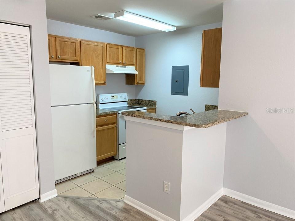 A kitchen features light wood cabinets, granite countertops, a white refrigerator, and tile flooring — 9045 LEE VISTA BOULEVARD UNIT 1502, ORLANDO, FL