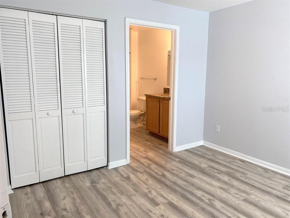 A bedroom with light gray walls, wood-look flooring, white louvered closet doors, and an attached bathroom — 9045 LEE VISTA BOULEVARD UNIT 1502, ORLANDO, FL