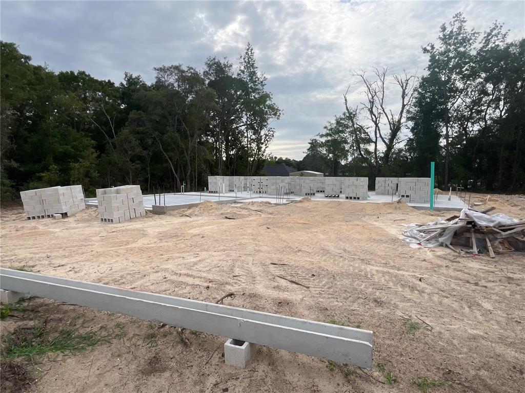 A construction site shows a partially built concrete block house with stacks of lumber nearby — 7 BAHIA PASS LANE, OCALA, FL