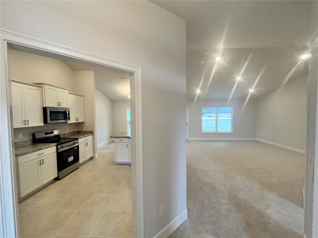 A kitchen with white cabinets and tile flooring opens into a carpeted living area — 7 BAHIA PASS LANE, OCALA, FL