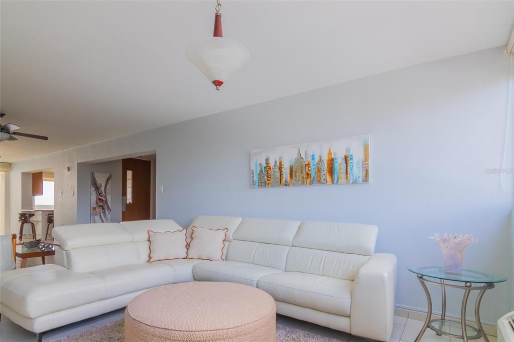 A living room features a white sectional sofa, a round ottoman, and a city skyline painting — 9550 CALLE DIAZ WAY | COND. ASTRALIS UNIT 813, CAROLINA, PR