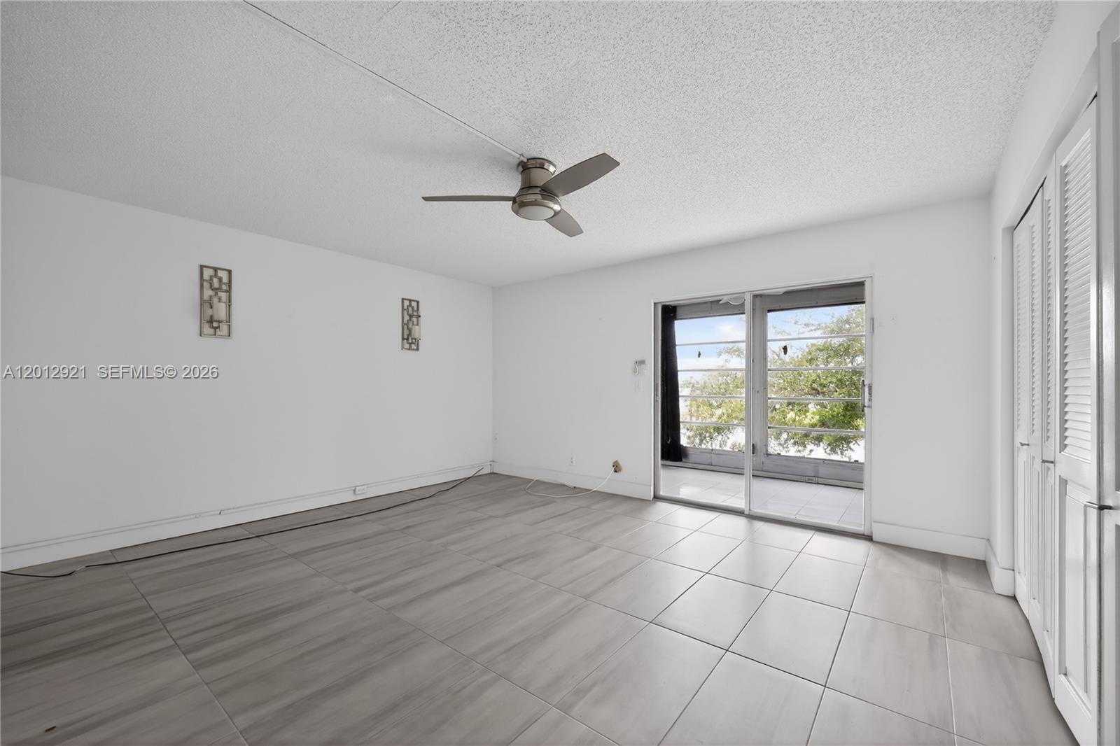 A bright, empty room features light-colored tile flooring, a ceiling fan, and sliding glass doors — 3023 Cambridge B # 3023, Deerfield Beach FL 33442, DEERFIELD BEACH, FL