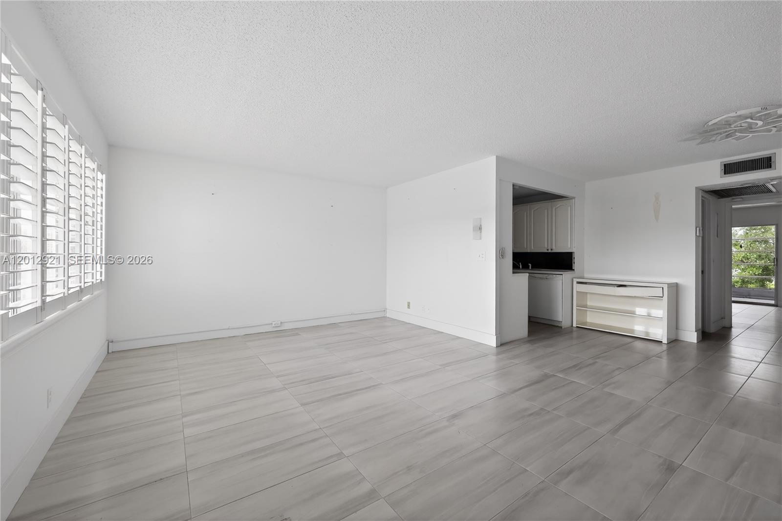 An empty living room features white walls, light-colored tile flooring, and a small kitchen pass-through — 3023 Cambridge B # 3023, Deerfield Beach FL 33442, DEERFIELD BEACH, FL