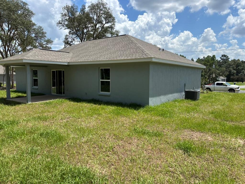 The rear exterior of a gray stucco house features a covered patio and yard — 659 W BANCROFT DRIVE, DUNNELLON, FL