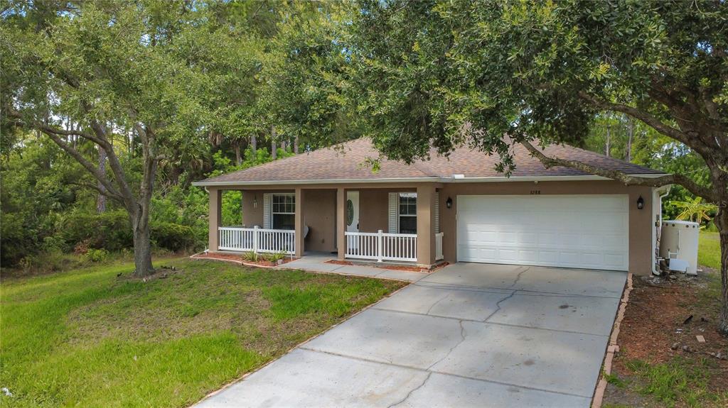 A single-story house with a white garage door, a covered porch, and surrounding trees — 3288 WALLACE AVENUE SE, PALM BAY, FL