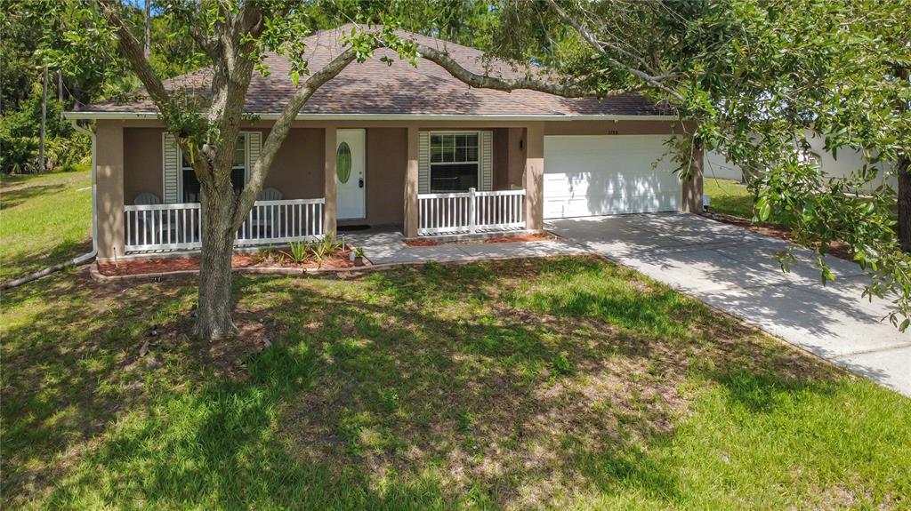 A single-story house with a white garage, front porch, and a large tree in front — 3288 WALLACE AVENUE SE, PALM BAY, FL