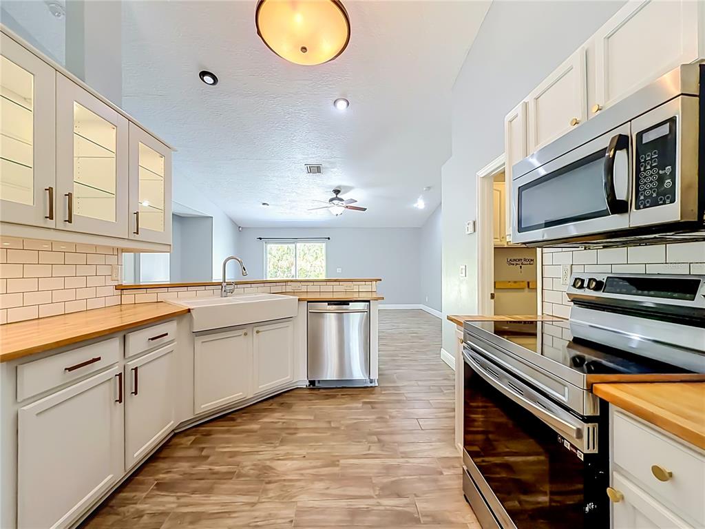 A kitchen features white cabinets, wood countertops, a farmhouse sink, and stainless steel appliances — 3288 WALLACE AVENUE SE, PALM BAY, FL