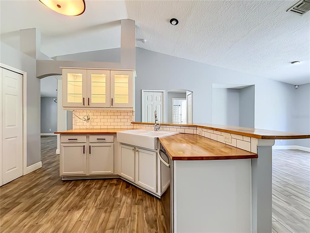 A kitchen features white cabinets, a farmhouse sink, wood countertops, and a subway tile backsplash — 3288 WALLACE AVENUE SE, PALM BAY, FL
