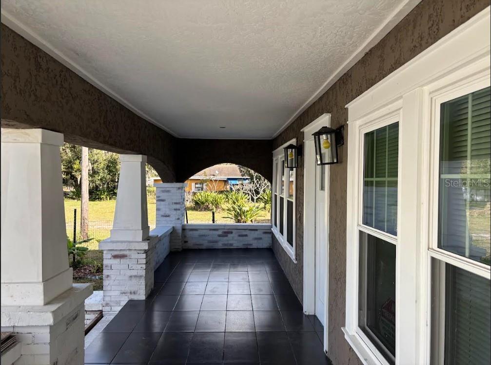 A covered porch features dark tiled flooring, white brick columns, and brown stucco walls — 2403 BURNS STREET, LAKELAND, FL
