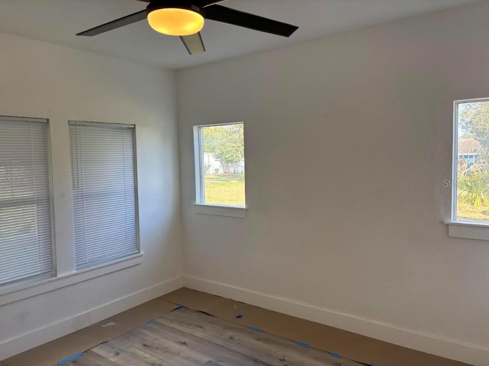 An empty room features white walls, light wood-look flooring, a ceiling fan, and multiple windows — 2403 BURNS STREET, LAKELAND, FL