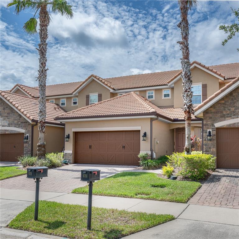 A two-story townhouse with a tan stucco exterior, stone accents, and a brown tile roof — 10751 BELFRY CIRCLE, ORLANDO, FL