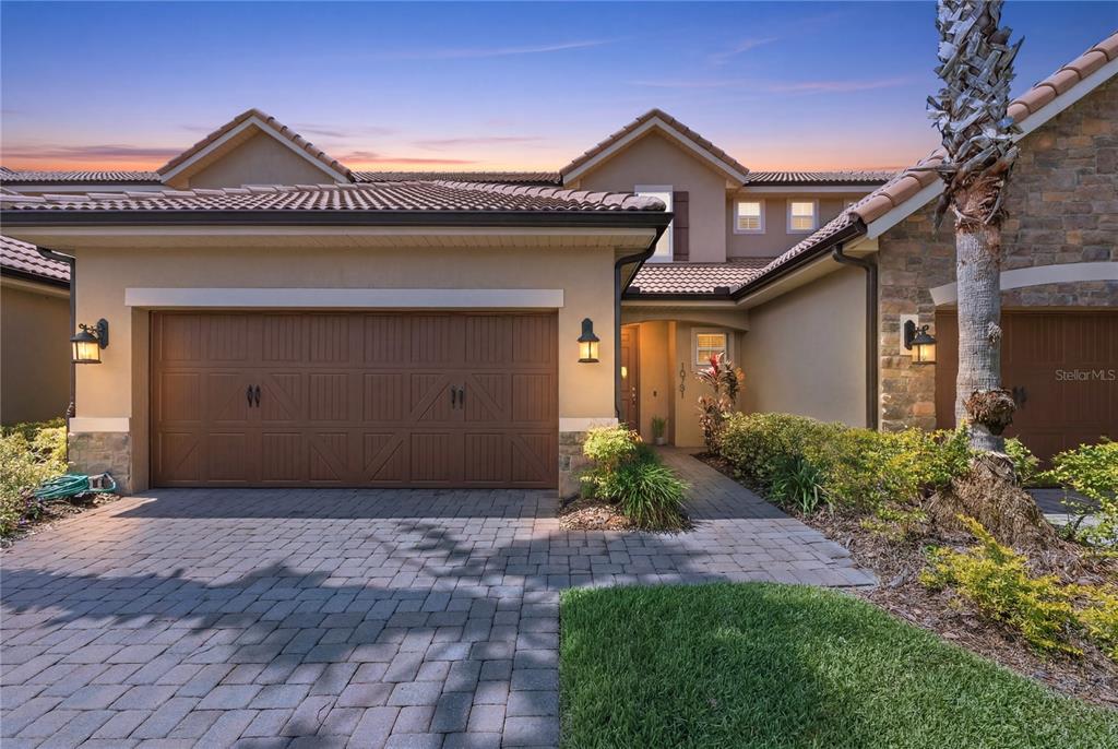 A tan stucco house with a brown garage door and a stone-accented entryway at dusk — 10751 BELFRY CIRCLE, ORLANDO, FL